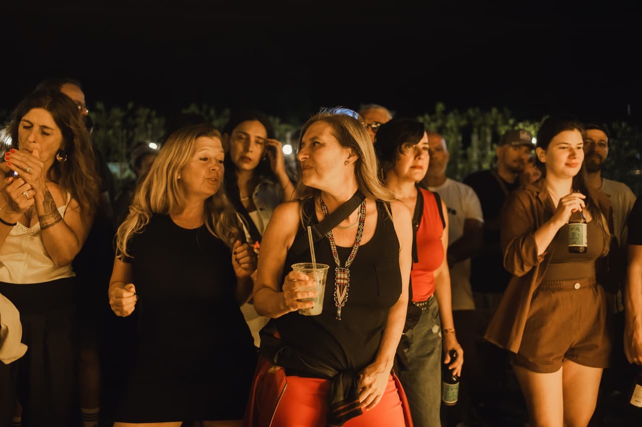 Pista ao ar livre à noite com grupo de pessoas dançando e conversando com copos na mão